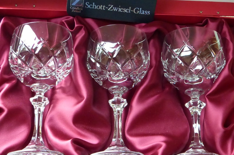 K&ouml;nnte beinhalten: Drei klare Weingl&auml;ser aus Glas mit einem Diamantenmuster auf einem roten Satinuntergrund. Die Gl&auml;ser befinden sich in einer Schachtel mit dem Logo Schott-Zwiesel-Glass.