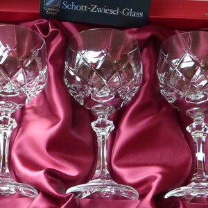 K&ouml;nnte beinhalten: Drei klare Glaskelche mit einem rautenf&ouml;rmigen Schliffmuster, pr&auml;sentiert in einer roten Samtbox mit dem Schriftzug "Schott-Zwiesel-Glass" auf dem Deckel.