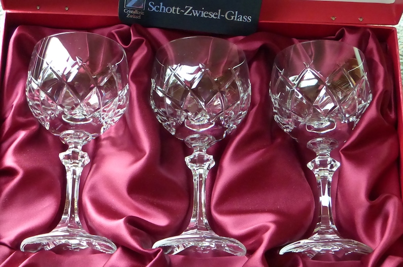K&ouml;nnte beinhalten: Drei klare Glaskelche mit einem rautenf&ouml;rmigen Schliffmuster, pr&auml;sentiert in einer roten Samtbox mit dem Schriftzug "Schott-Zwiesel-Glass" auf dem Deckel.
