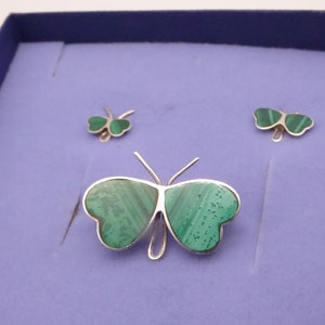 May include: A silver butterfly brooch with green malachite wings. The brooch is displayed in a blue velvet box with two matching earrings.