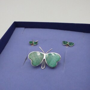 May include: A set of three silver butterfly earrings with green malachite stones. The earrings are displayed in a blue velvet box.