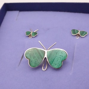 May include: A set of three silver butterfly jewelry pieces with green malachite stone accents. The largest piece is a brooch, and the smaller pieces are earrings.