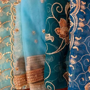 May include: Four pieces of fabric with intricate embroidery in shades of blue and gold. The fabric is sheer and delicate, with a variety of floral and geometric patterns.