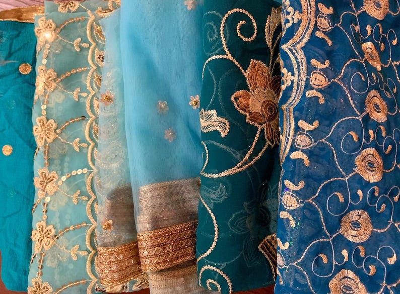 May include: Four pieces of fabric with intricate embroidery in shades of blue and gold. The fabric is sheer and delicate, with a variety of floral and geometric patterns.
