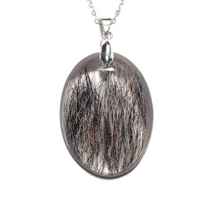 May include: A silver necklace featuring an oval pendant with a clear, transparent appearance. The pendant is filled with black and silver needle-like inclusions, creating a unique, textured effect. The chain is delicate and silver.
