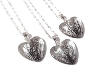 May include: Three heart-shaped pendants with silver chains. Each pendant has a clear, heart-shaped resin with black strands inside. The chains and pendant attachments are silver. The pendants are displayed against a white background.