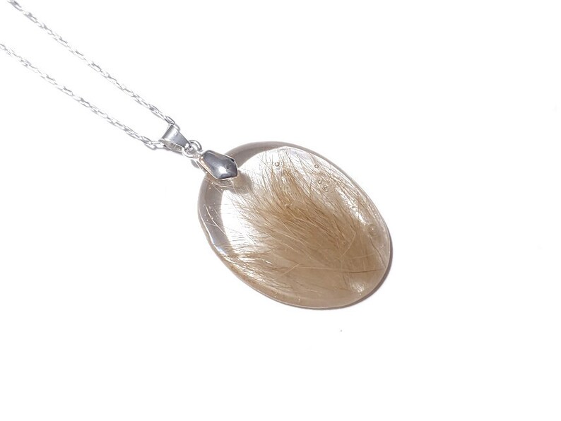 May include: A clear, oval-shaped pendant necklace with a silver chain. The pendant contains golden-brown inclusions, creating a unique, natural appearance. The necklace is displayed against a white background, highlighting the pendant's details.