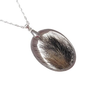 May include: Oval pendant necklace with a clear resin stone, featuring black and brown inclusions. The pendant is suspended from a delicate silver chain. The necklace is displayed against a white background, highlighting the pendant's unique design.