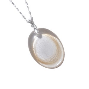 May include: A silver necklace with a clear, oval pendant. The pendant contains a swirl of light brown hair. The chain is delicate and the pendant is smooth and polished.