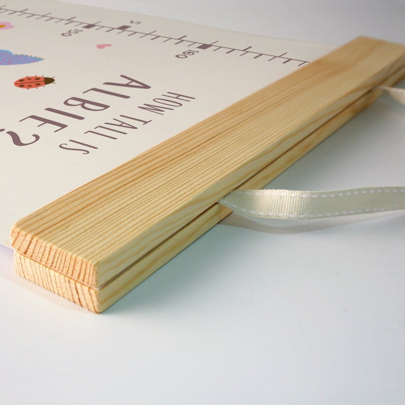 May include: A wooden growth chart with a white background and a light brown wooden frame. The chart has a white ribbon attached to the frame. The text "How Tall Is Albie?" is printed on the chart.