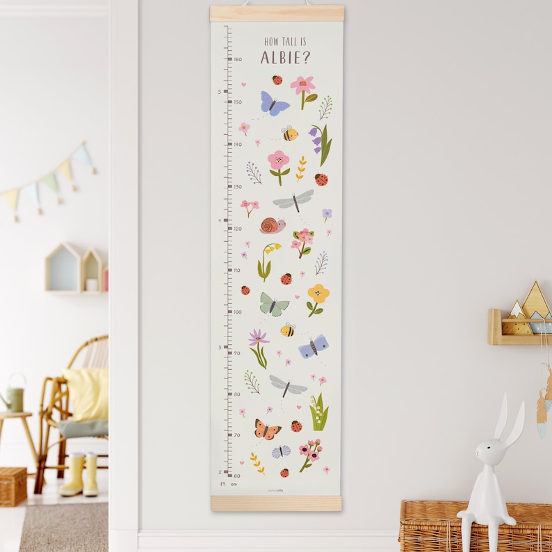 May include: A white growth chart with a wooden frame and a colorful floral design. The chart features butterflies, bees, ladybugs, and other insects. The text "How tall is Albie?" is printed at the top of the chart.