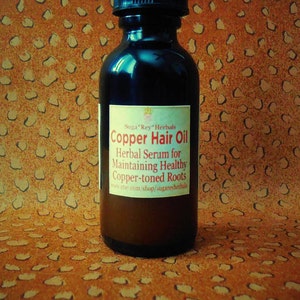 May include: A dark brown glass bottle with a black dropper top. The bottle is labeled "Copper Hair Oil" and "Herbal Serum for Maintaining Healthy Copper-toned Roots". The label also includes the website "www.etsy.com/shop/sugaresferhels".