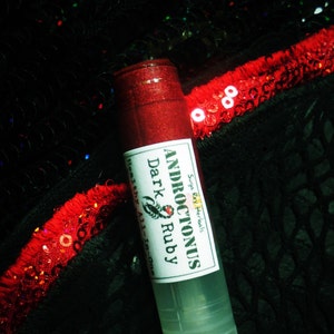 May include: A clear tube containing a red, glittery lip balm. The tube is labelled with "ANDROCTONUS Dark Ruby Healthy All-in-one" and a small scorpion graphic.