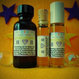 May include: Three glass bottles with cork stoppers and labels. The labels are white with black text and a diamond design. The text on the labels reads "gemInIgem" and "Anointing oil to bless the mercurial Gemini with wisdom & contentment as we soar among our many sides, differences, & ideas."