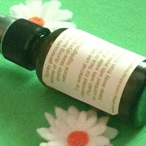 May include: A clear glass bottle with a black spray nozzle and a white label. The label has text that reads "Spray generously before or during sun and/or blow-drying natural highlights" and "For external use on intended for face or body. Flush with water if in contact with eyes. Keep away from children. www.etsy.com/shop/sugarplum",  The bottle is sitting on a green surface.