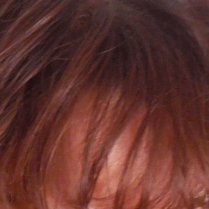 May include: Close-up of a person's face with brown hair covering part of their forehead. One eye is visible, with brown eyelashes and a green iris.