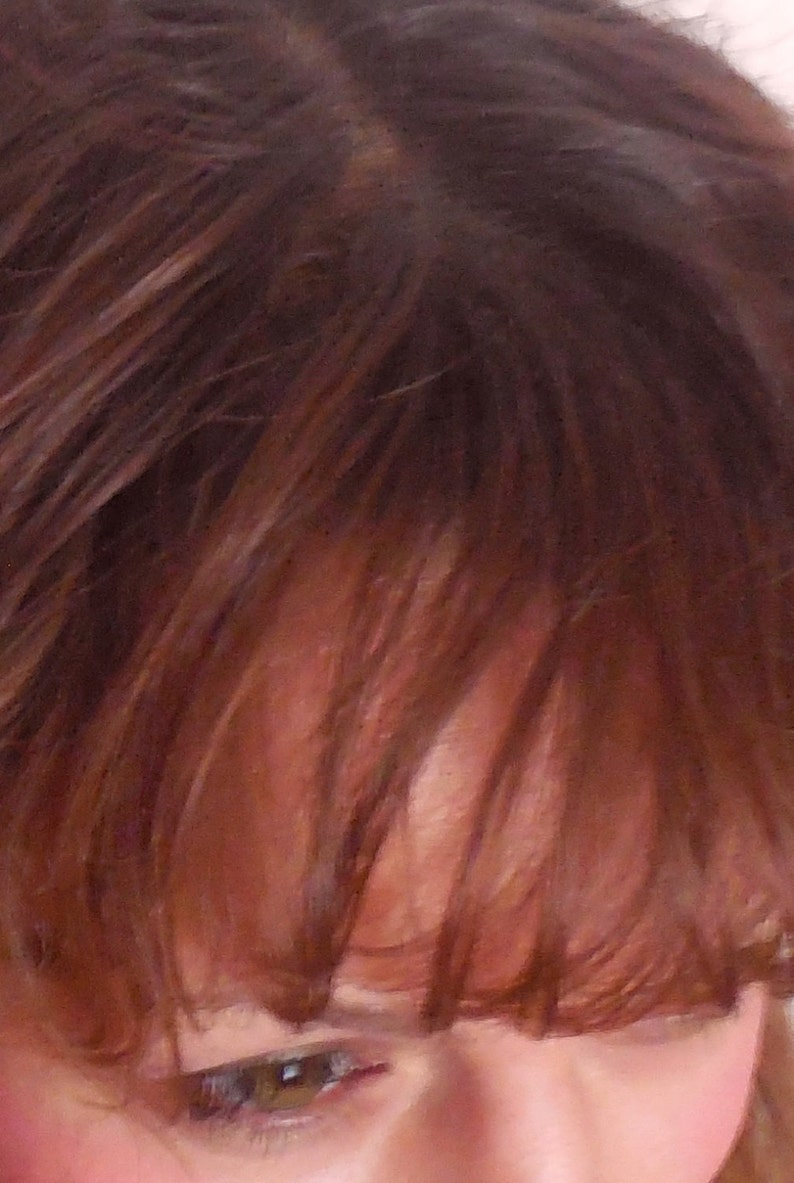 May include: Close-up of a person's face with brown hair covering part of their forehead. One eye is visible, with brown eyelashes and a green iris.