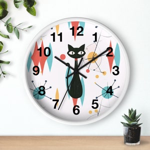 May include: White analog clock with black numbers and a black cat design. The cat is in the center of the clock and has a red collar. The background of the clock is a white and blue geometric pattern.
