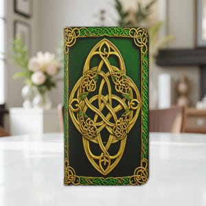 Może przedstawiać: Prostokątne etui z zielono-złotym wzorem celtyckiego węzła. Złożona złota praca węzłowa osadzona jest na ciemnozielonym tle, obramowanym zieloną obwódką ze złotymi detalami. Etui jest prawdopodobnie przeznaczone na telefon lub podobne urządzenie.