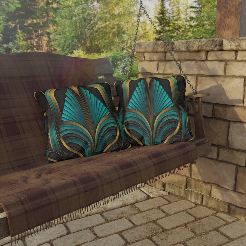 May include: Two teal and gold art deco-style throw pillows on a brown wooden swing. The pillows feature a repeating geometric pattern with teal, gold, and black accents. The swing is outdoors on a stone patio.