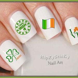 Könnte beinhalten: Vier weiße Fingernägel mit grünen Kleeblatt-Designs. Ein Nagel hat ein grünes Kleeblatt mit dem Wort "IRISH" in orangefarbenen Buchstaben. Ein anderer Nagel hat ein grünes Kleeblatt mit den Worten "LOVE" in grünen Buchstaben. Ein weiterer Nagel hat ein grünes Kleeblatt mit den Worten "100% IRISH" in grünen Buchstaben. Der letzte Nagel hat ein grünes, weißes und orangefarbenes irisches Flaggen-Design. Der Text "HipZySticky Nail Art" ist unter den Fingernägeln gedruckt.