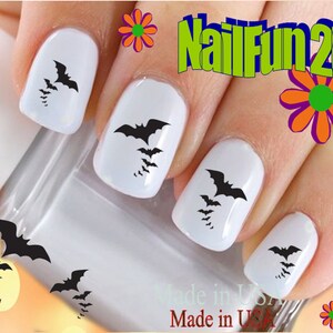 May include: Black bat nail decals on white painted fingernails. The decals are in various sizes and are arranged in a cluster on each fingernail. The image includes the text "NailFun2U".