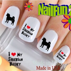 Puede incluir: Calcomanías para uñas con una silueta negra de un perro Husky siberiano y el texto "Me encanta mi Husky siberiano" con un corazón rojo. Las calcomanías se muestran en uñas pintadas de blanco.