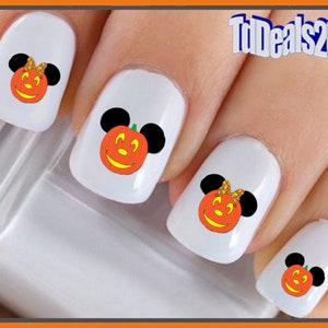 May include: Four white fingernails with Halloween-themed nail art featuring Mickey Mouse and Minnie Mouse dressed as pumpkins. The nail art is orange, black, and yellow.