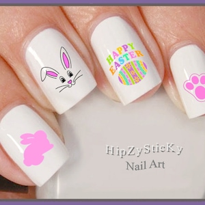 以下が含まれることがあります： ピンクのウサギ、足跡、ウサギのシルエット、そして「ハッピーイースター」の文字が入ったカラフルなイースターエッグが描かれたイースターネイルアートステッカーです。