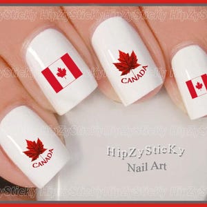 May include: White nail polish base with Canada-themed nail art decals. The designs include the red and white Canadian flag and a red maple leaf graphic with the text "CANADA" printed in red. The text "HipZySticKy Nail Art" is visible.