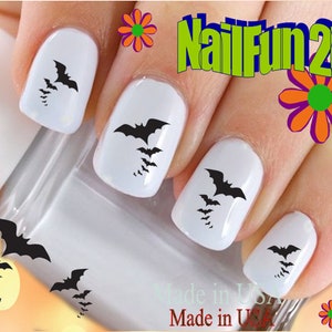 May include: Black bat nail decals on white painted fingernails. The decals are in various sizes and are arranged in a cluster on each fingernail. The image includes the text "NailFun2U".