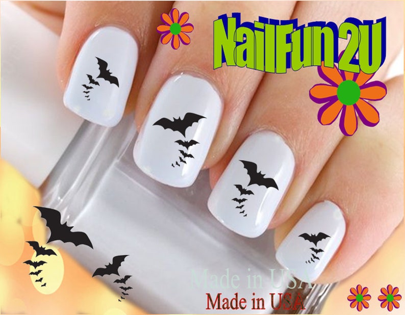 May include: Black bat nail decals on white painted fingernails. The decals are in various sizes and are arranged in a cluster on each fingernail. The image includes the text "NailFun2U".