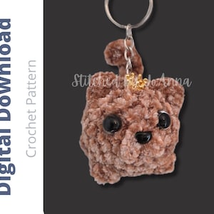 May include: A brown crocheted plush keychain shaped like a small animal with large black plastic eyes and a black nose. A small gold-colored crown sits on its head. The text Digital Download Crochet Pattern Stitched By JoAnna is visible.