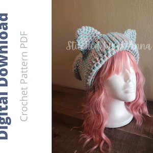 May include: A digital download crochet pattern PDF for a cat ear hat. The hat is a mix of light blue and pink yarn, with two cat ears on top. The hat is displayed on a white mannequin head with pink hair.