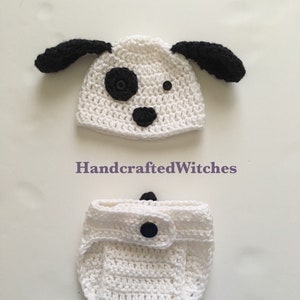 May include: White crocheted baby hat and diaper cover with black ears, nose, and eyes. The hat has a black spot on the side. The diaper cover has a black button. "HandcraftedWitches" is written on the image. "Color: white" is written at the bottom of the image.