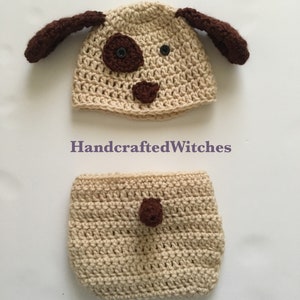 May include: A crocheted dog hat and diaper set in light brown with brown accents. The hat has floppy ears and a face with a nose, eyes, and a spot. The diaper has a single spot on the front.