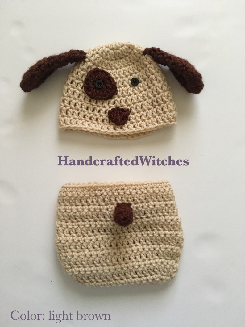 May include: A crocheted dog hat and diaper set in light brown with brown accents. The hat has floppy ears and a face with a nose, eyes, and a spot. The diaper has a single spot on the front.