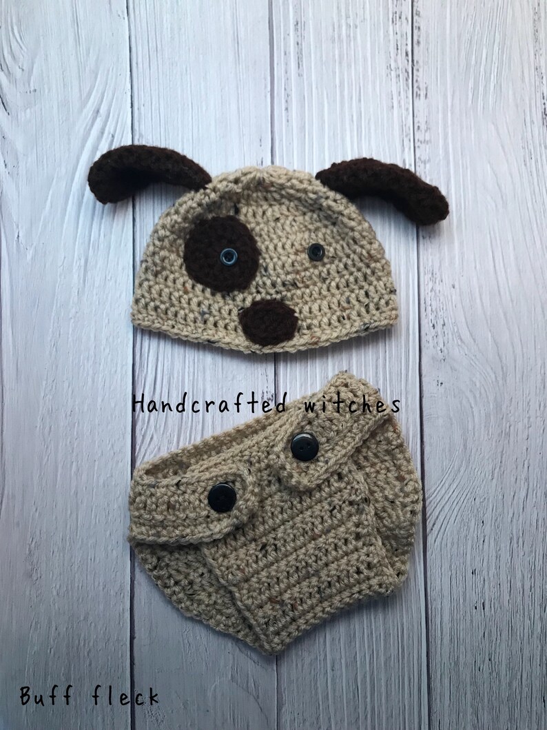 May include: A crocheted dog hat and diaper set in beige and brown with black buttons. The hat has brown ears and a brown nose with blue eyes. The diaper has two black buttons. The set is handcrafted.