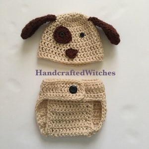 May include: A crocheted dog hat and diaper set in light brown with black buttons. The hat has brown ears and a brown nose and eyes. The diaper has a button closure. HandcraftedWitches.
