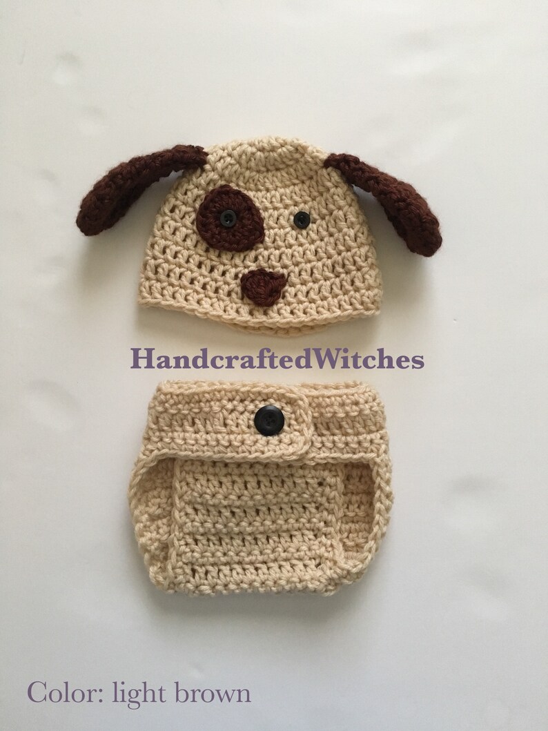 May include: A crocheted dog hat and diaper set in light brown with black buttons. The hat has brown ears and a brown nose and eyes. The diaper has a button closure. HandcraftedWitches.