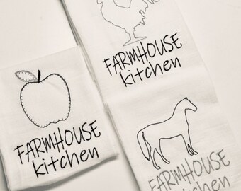 May include: Three white kitchen towels with black embroidery. The towels feature a rooster, an apple, and a horse, each with the text "Farmhouse Kitchen".