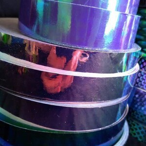 May include: A stack of iridescent purple and blue vinyl tape rolls. The tape is holographic and has a reflective finish.