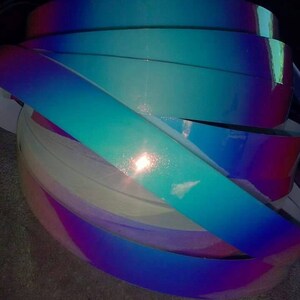 Puede incluir: Un rollo de vinilo iridiscente en tonos azules, morados y rosas. El vinilo tiene un acabado hologr&aacute;fico que brilla a la luz.