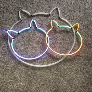 May include: Two neon cat head outlines, one blue and green, the other orange and yellow, are intertwined on a gray carpet.