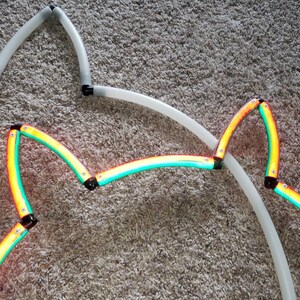 May include: A close-up of a multi-colored star-shaped light. The light is made of flexible tubing and is connected together with black connectors. The light is lit up in a rainbow of colors, including red, orange, yellow, green, blue, indigo, and violet.