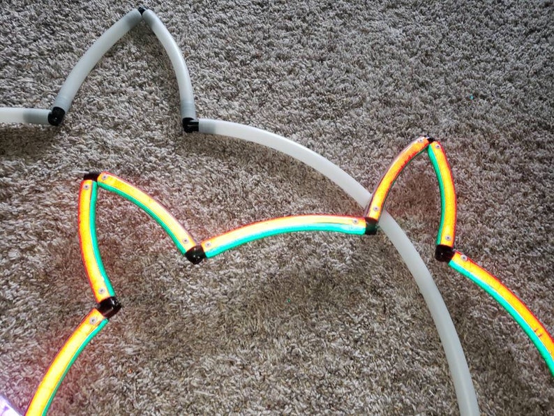 May include: A close-up of a multi-colored star-shaped light. The light is made of flexible tubing and is connected together with black connectors. The light is lit up in a rainbow of colors, including red, orange, yellow, green, blue, indigo, and violet.
