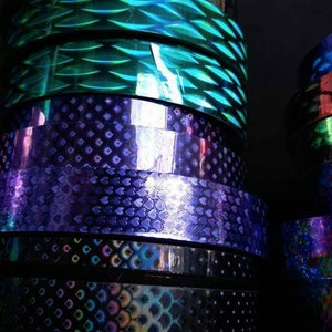 May include: Rolls of iridescent holographic vinyl tape in various colors and patterns, including green, purple, and blue.