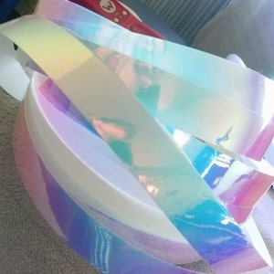 Puede incluir: Primer plano de rollos de cinta de vinilo hologr&aacute;fica iridiscente. La cinta es un arco&iacute;ris de colores, incluyendo rosa, azul, verde y morado.