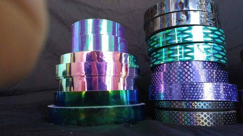 May include: Assortment of iridescent holographic tape rolls in various colors and patterns, including purple, green, and blue.