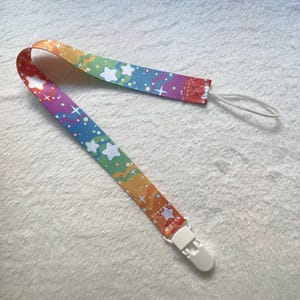 May include: A rainbow-colored pacifier clip with white stars and a white plastic clip. The clip is attached to a white string.